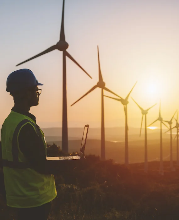 ingénieur freelance - un homme avec un ordinateur portable devant un champ d'éoliennes sur fond de soleil levant
